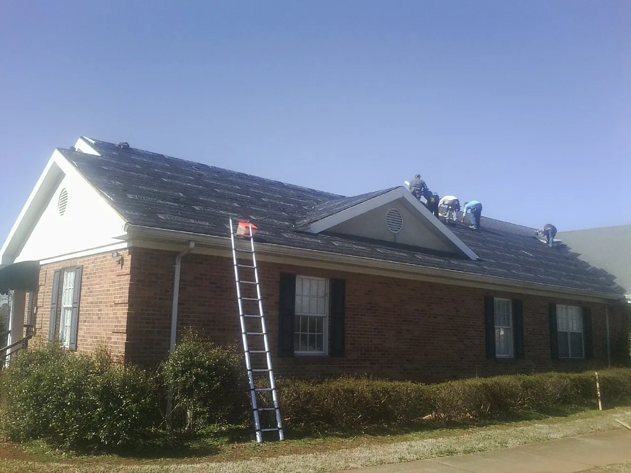 Crew tearing shingles off a brick ranch roof with a ladder set — Emergency Roof Repair work by our crew in Agra