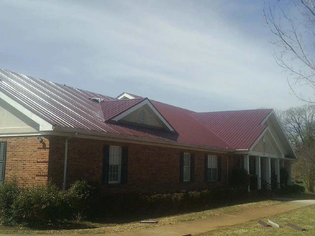 Red metal roof with gabled entries on a long brick building, from a Hail Damage Roof Repair job in Agra