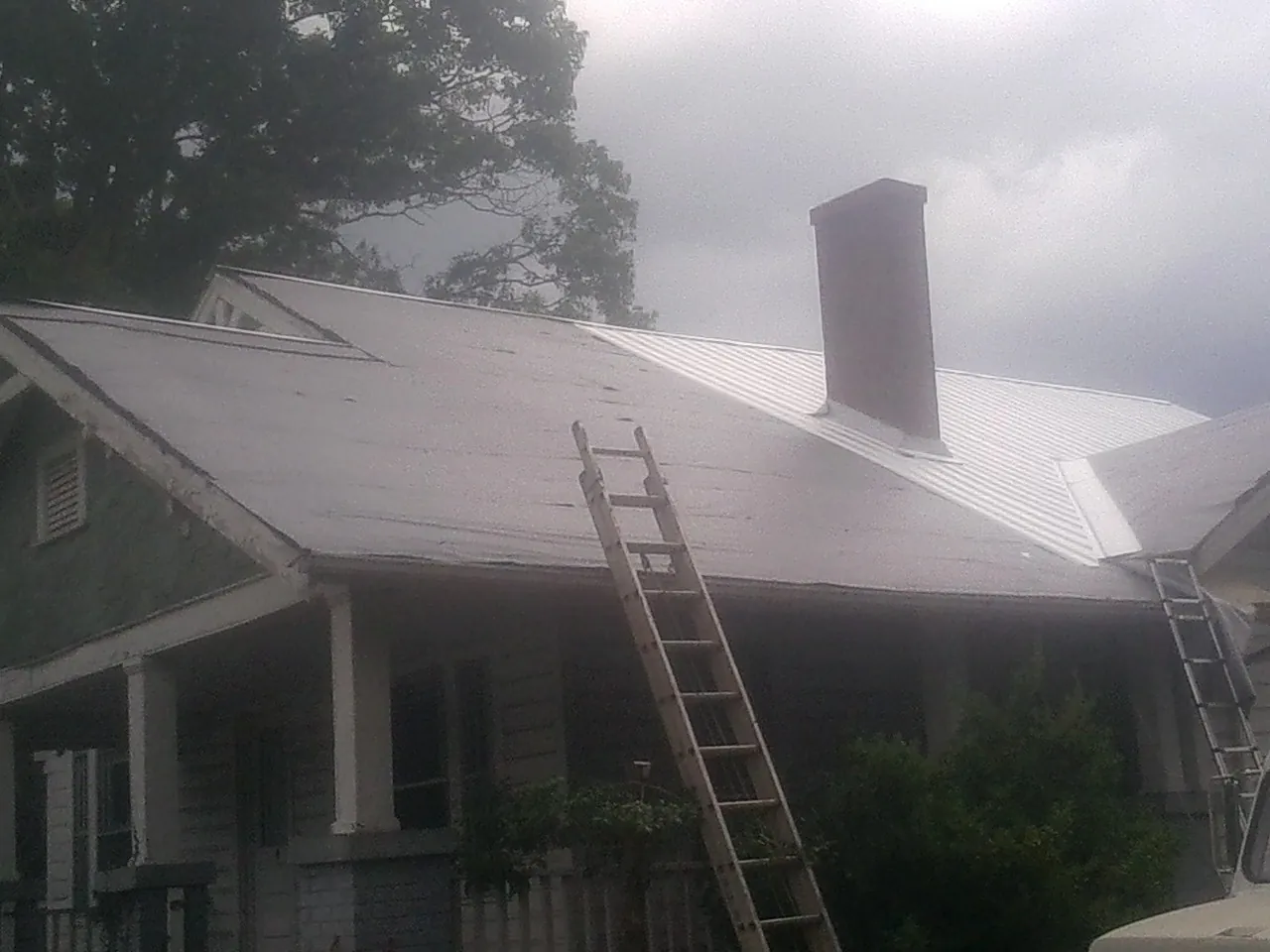 Ladders against a metal roof on an older home with a brick chimney in Agra