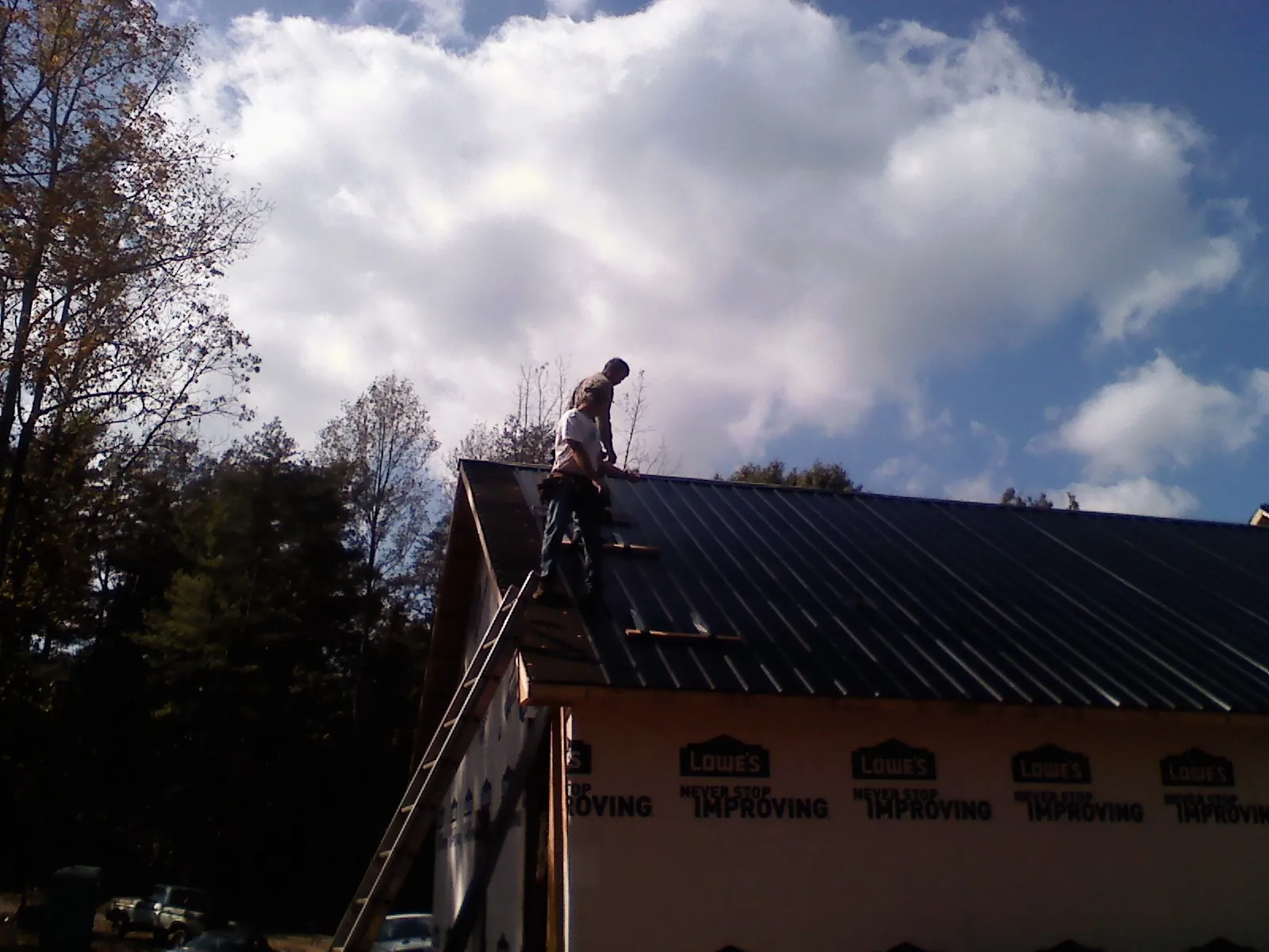Roofer fastening dark metal panels high against a cloudy sky, from a Roof Inspection job in Agra