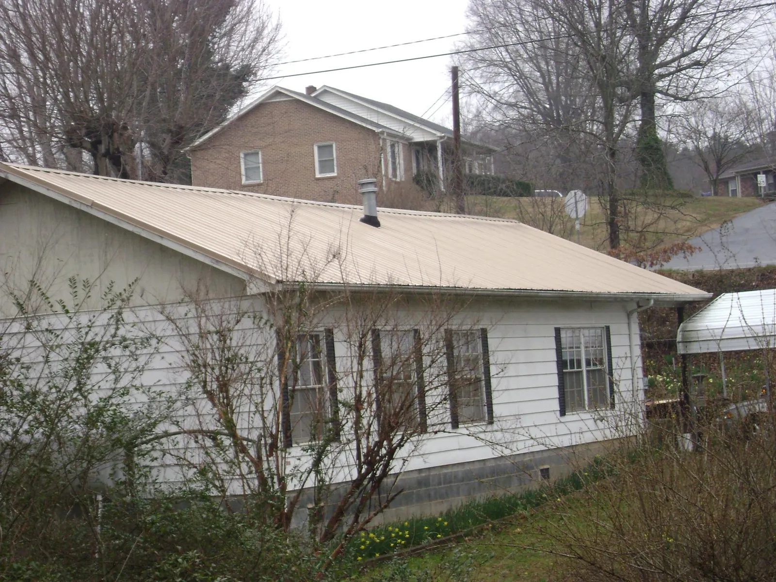 Tan metal roof on a white sided house set into a hillside — Commercial Roofing by Roofing Brothers in Agra